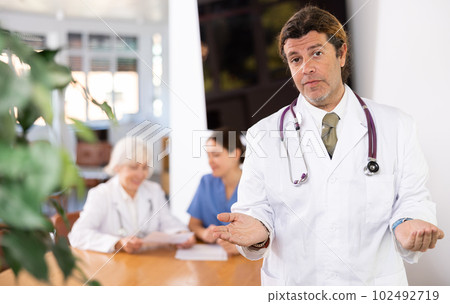 Professional doctor politely inviting patients in medical office 102492719