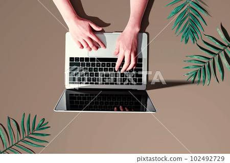 Person using a laptop computer with tropical leaves 102492729