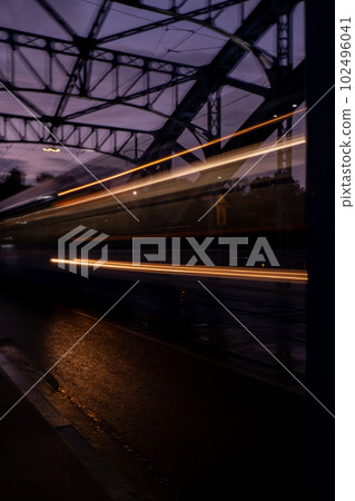 Defocused Lights of cars at night in Krakow bridge. Street line lights. Night highway city. Long exposure photograph night road. Colored bands of red light trails on the road. Background wallpaper Defocused Lights of cars at night in Krakow bridge. Street line lights. Night highway city. Long exposure photograph night road. Colored bands of red light trails on the road. Background wallpaper 102496041
