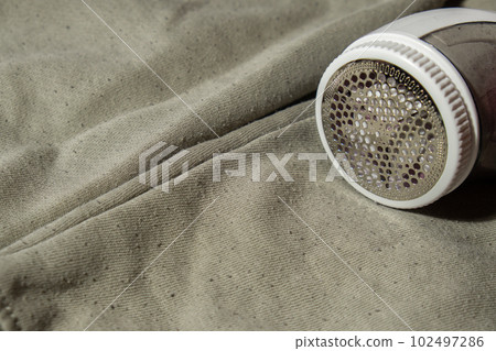 Anti-pilling razor. Device for shaving pellets clothes. Anti-Plush fabric Shaver. Electric portable sweater pill defuzzer Lint remover from acrylic or wool sweater. Sustainability lifestyle fashion Anti-pilling razor. Device for shaving pellets clothes. Anti-Plush fabric Shaver. Electric portable sweater pill defuzzer Lint remover from acrylic or wool sweater. Sustainability lifestyle fashion 102497286