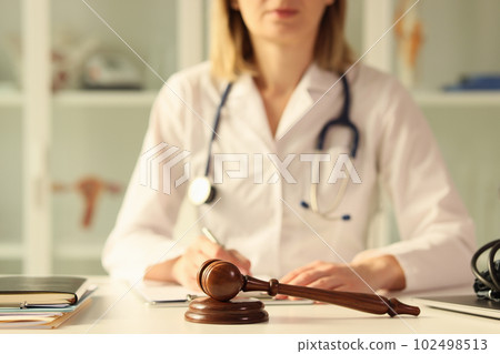 Wooden judge gavel on table female doctor doing paperwork on background Wooden judge gavel on table female doctor doing paperwork on background 102498513
