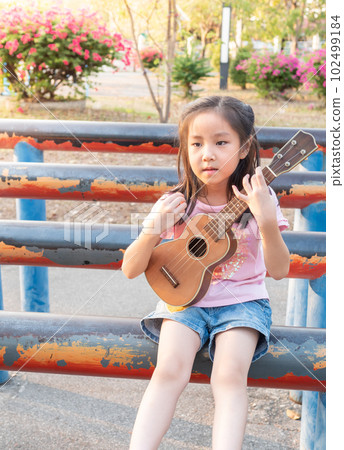 Little asian child girl play the ukulele, in the garden on the Steel pipe 102499184