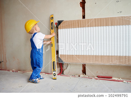 Full length of baby boy in workwear using spirit level ruler while installing heating radiator in apartment under renovation. Kid checking wall and radiator heater with precision measuring device. Full length of baby boy in workwear using spirit level ruler while installing heating radiator in apartment under renovation. Kid checking wall and radiator heater with precision measuring device. 102499791