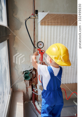 Kid using air compressor manometer while checking gas tightness of radiator in apartment under renovation. Child filling pipes with pressurized air to inspect for leaks in heating system. 102499830