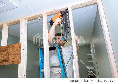 Builder uses an air hammer to nail wooden beams framework for construction of house Builder uses an air hammer to nail wooden beams framework for construction of house 102500358