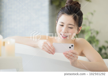 Female beauty A young woman looking at her smartphone while taking a bath 102501292
