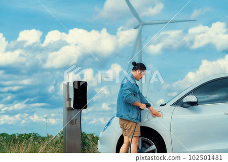 Progressive man with his EV car and wind turbine as concept of renewable energy. 102501481
