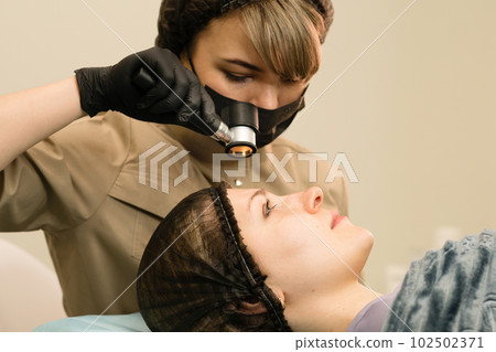 Dermatologist examines moles with dermatoscope 102502371