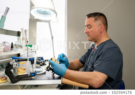 Dental technician working with tooth denture 102504178