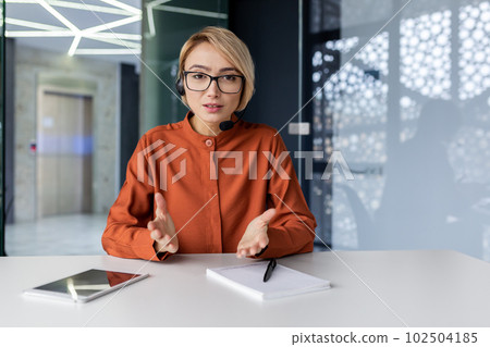 Serious business woman talking to a video call report, thoughtfully looking at the web camera, female employee working inside the office of an online customer service support tech Serious business woman talking to a video call report, thoughtfully looking at the web camera, female employee working inside the office of an online customer service support tech 102504185