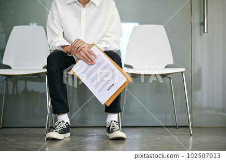 Cropped image of a young male candidate sits in a waiting room with his resume. Cropped image of a young male candidate sits in a waiting room with his resume. 102507013