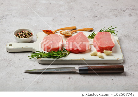 Three uncooked pork cutlets on cutting board Three uncooked pork cutlets on cutting board 102507742