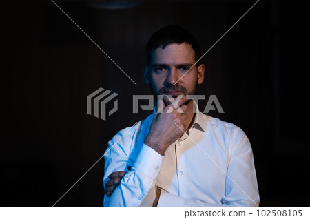 A bearded man stands in the dark and looks ahead puzzled. A bearded man stands in the dark and looks ahead puzzled. 102508105