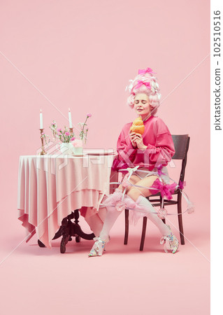 Portrait with dreaming princess, queen wearing big wig and starting eat huge croissant on pink background with astonished face 102510516