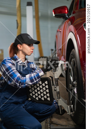 A female auto mechanic makes a camber. Woman working in a car service. 102510917