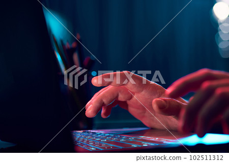 Businessman working remotely, typing on laptop keyboard over neon lights. Working with online projects 102511312