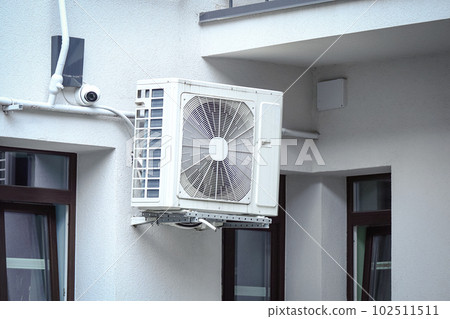 Air condition outdoor unit compressor installed outside the house hanging on a wall between windows Air condition outdoor unit compressor installed outside the house hanging on a wall between windows 102511511