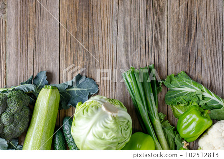 Border of green raw vegetables on wooden background. Top view of healthy organic food. Copy space 102512813