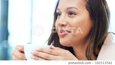 Woman drinking a hot cup of tea or coffee at home. Face of a carefree young female smelling the aroma of a fresh warm beverage while taking a sip and relaxing at home. Enjoying a comfortable break 102513582