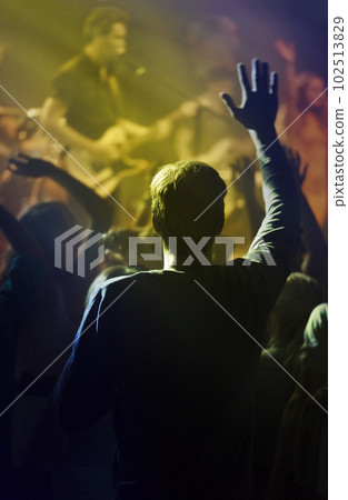 Concert, singing and people dancing to music at night performance, rock and gen z singer in lights and cheers. Musician on stage at disco event and fans rear, crowd or audience with man hands in air 102513829