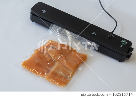 Vacuum packaging machine packs salmon fillets in a vacuum bag for pickling or sous-vide cooking Vacuum packaging machine packs salmon fillets in a vacuum bag for pickling or sous-vide cooking 102515714