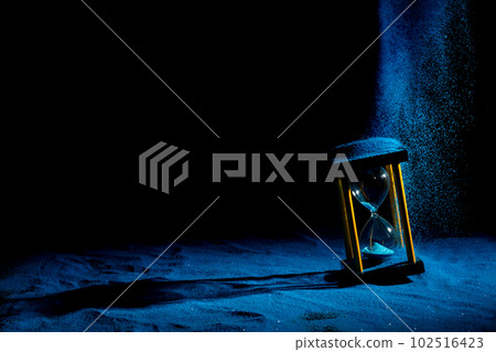 Hourglass is sand of time age, Life pour blue sand into hourglass to add more limited time. Deadline extended time management hope concept hour glass. Black background shadow life clock passing by 102516423
