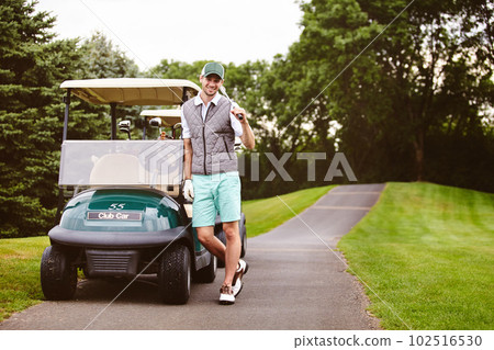 Im really enjoying this. Full length portrait of a handsome young man leaning against a golf cart on a golf course. 102516530