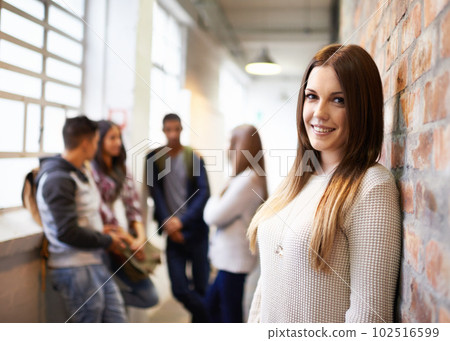 Education always puts a smile on my face. Portrait of a beautiful young female student leaning against a brick wall with her friends in the background. Education always puts a smile on my face. Portrait of a beautiful young female student leaning against a brick wall with her friends in the background. 102516599