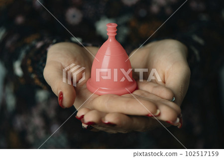 woman holding a pink menstrual cup in her hands 102517159
