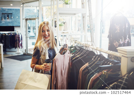 Sometimes you just need to spoil yourself. a young woman holding up an item that she picked out in a clothing store. 102517464