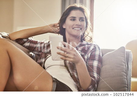Theres no substitute for a chilled out sofa day. a young woman relaxing on the sofa at home and using a mobile phone. 102517844
