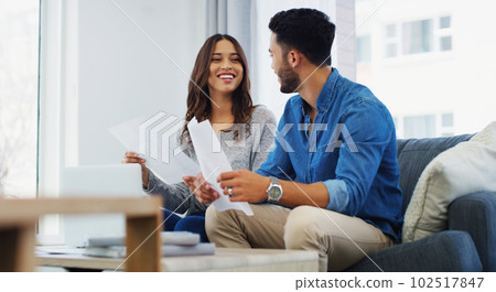 Im going to hide the bill for those shoes. an happy young couple sitting on the sofa while going through paperwork in their lounge. 102517847
