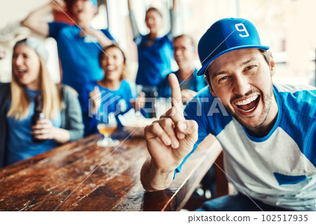 Weve been reigning champions since day one. Portrait of a man holding up one finger while watching a sports game with friends at a bar. 102517935