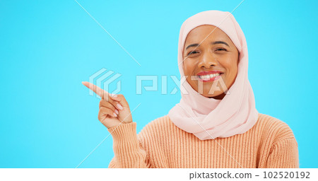 Woman, pointing finger and space for happy muslim announcement with hand for mockup. Islamic female with hijab and face with smile for sale, promotion or product placement on studio blue background 102520192