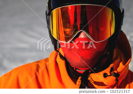Portrait of a man with yellow eyes. Photo of a young serious sportsman in a helmet and ski goggles in his hands, against the backdrop of a snowy hill 102521357