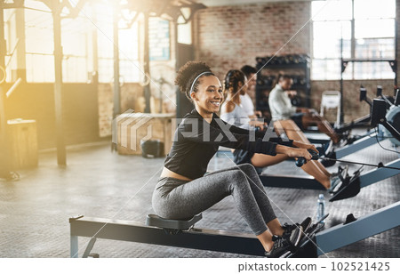 Group, rowing machine and training in gym, class or fitness workout, exercise or cardio, row team and practice. People, healthy athlete and challenge on sport equipment, row crew and sports club 102521425