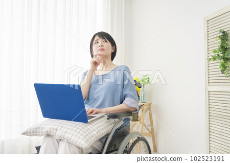 A woman in a wheelchair thinking while using a laptop in the living room A woman in a wheelchair thinking while using a laptop in the living room 102523191