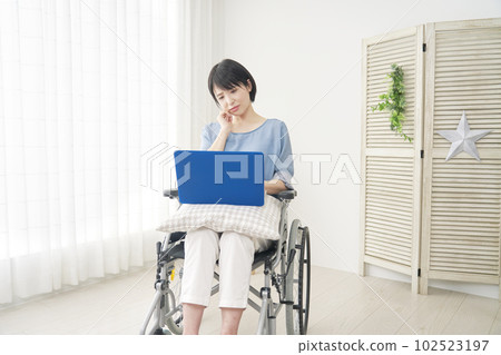 A woman in a wheelchair who is worried while using a laptop in the living room 102523197