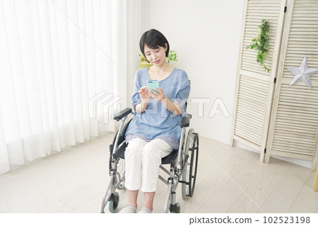 坐在輪椅上的女人在客廳裡使用智能手機 坐在輪椅上的女人在客廳裡使用智能手機 102523198