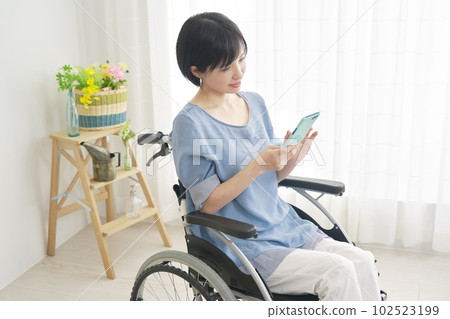坐在輪椅上的女人在客廳裡使用智能手機 坐在輪椅上的女人在客廳裡使用智能手機 102523199