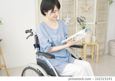 A woman in a wheelchair reading in the living room 102523241