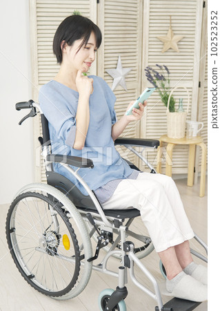 坐在輪椅上的女人在客廳裡使用智能手機 坐在輪椅上的女人在客廳裡使用智能手機 102523252