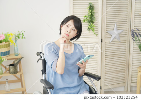 A woman in a wheelchair thinking while using a smartphone in the living room 102523254