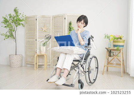 A woman in a wheelchair thinking while using a laptop in the living room A woman in a wheelchair thinking while using a laptop in the living room 102523255