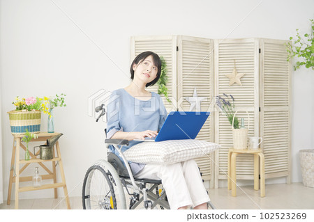 A woman in a wheelchair imagining while using a laptop in her living room 102523269