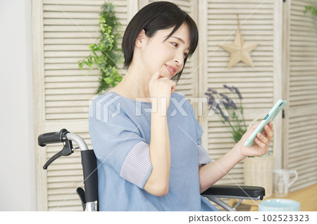 A woman on a wheelchair using a smartphone in the living room 102523323