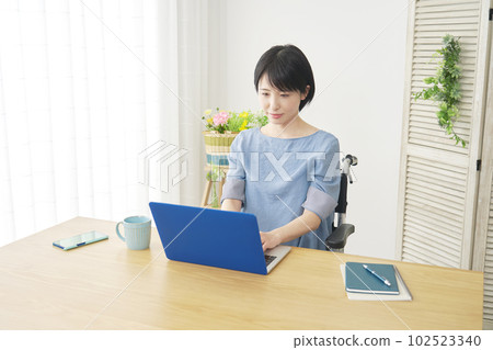 坐在輪椅上的女人在客廳裡使用筆記本電腦 坐在輪椅上的女人在客廳裡使用筆記本電腦 102523340