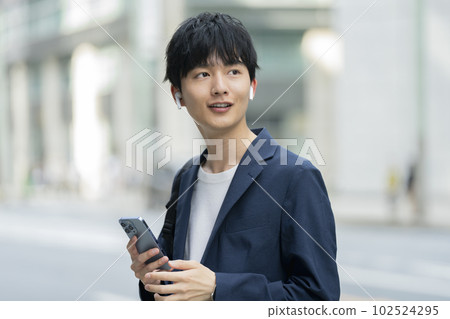 A man in his twenties holding a smartphone and wearing wireless earphones A man in his twenties holding a smartphone and wearing wireless earphones 102524295