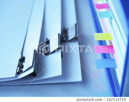 A blue file on a table and papers bound with clips 102524710