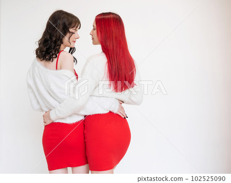 Rear view of two women dressed in identical red dresses and white sweaters. Lesbian intimacy. White background. Rear view of two women dressed in identical red dresses and white sweaters. Lesbian intimacy. White background. 102525090